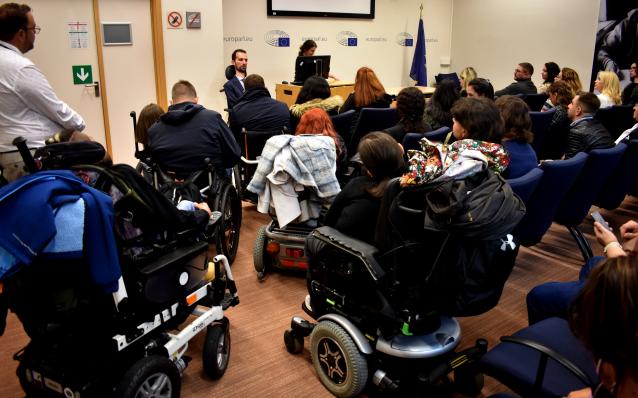 photo in the enclosed space of the European parliament, in the speakers position there are two people, a man (Kimpouropoulos) and a woman in fron of an audience of disabled and able-bodied people.
