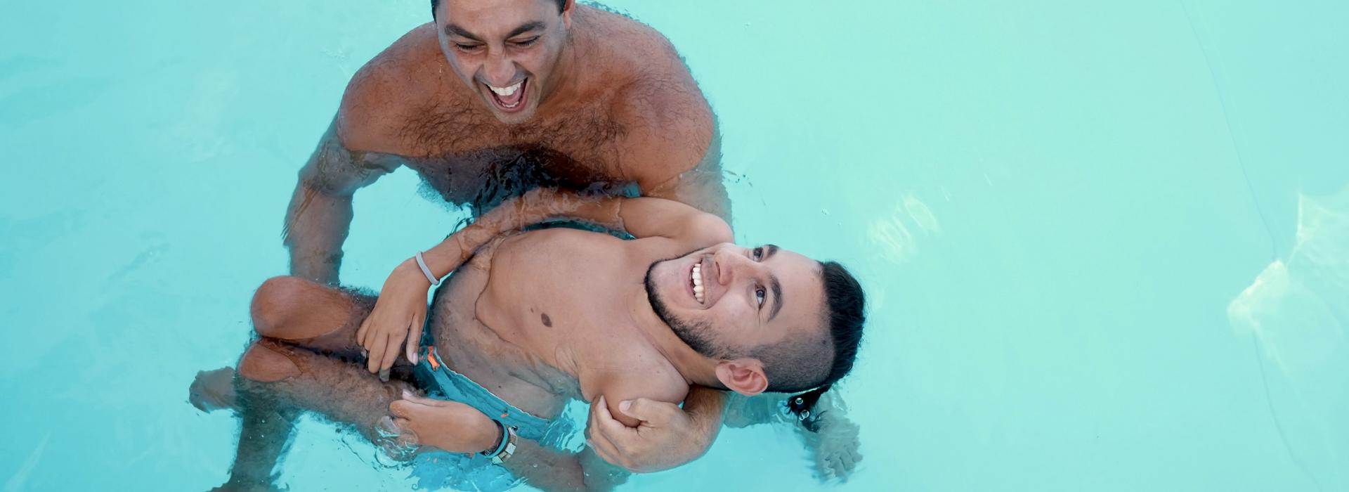 Cover. 35 years old man and 20 years old disabled man laughing in a swimming pool.