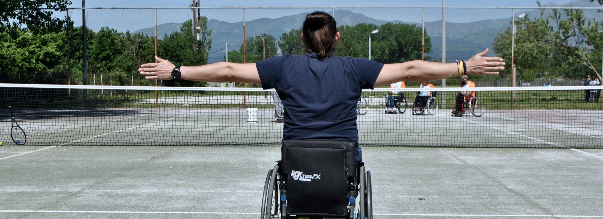 Cover. Tennis court. Back of a male wheelchair user stretching his arms left and right on the same line with the horizon.