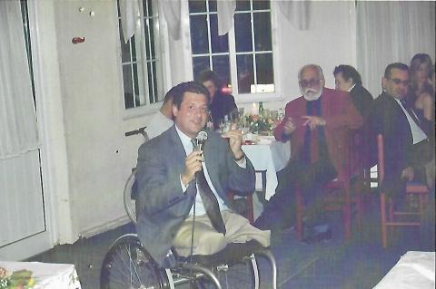 photo of a man who is a wheelchair user and speaks using a mic. the photo is old (approximately 2002)