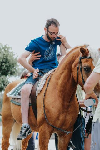 photo of a man who is disabled and he is riding a horse while supported by many people’s hands.